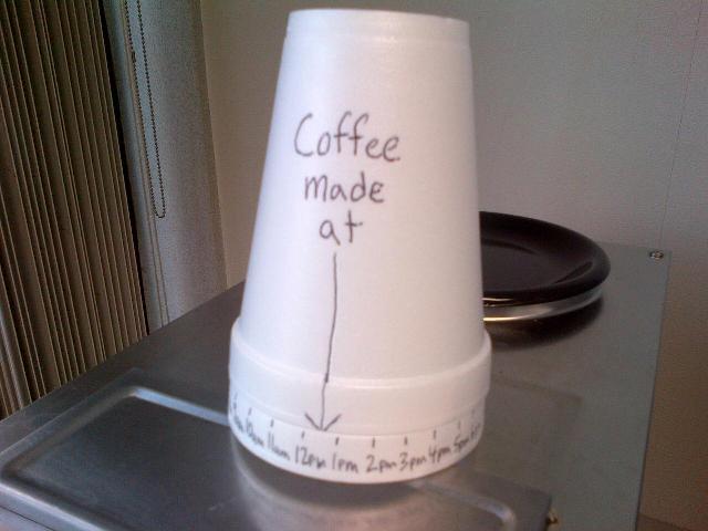A device made from two coffee cups, one with times on its rim held by another with an arrow pointing at the times